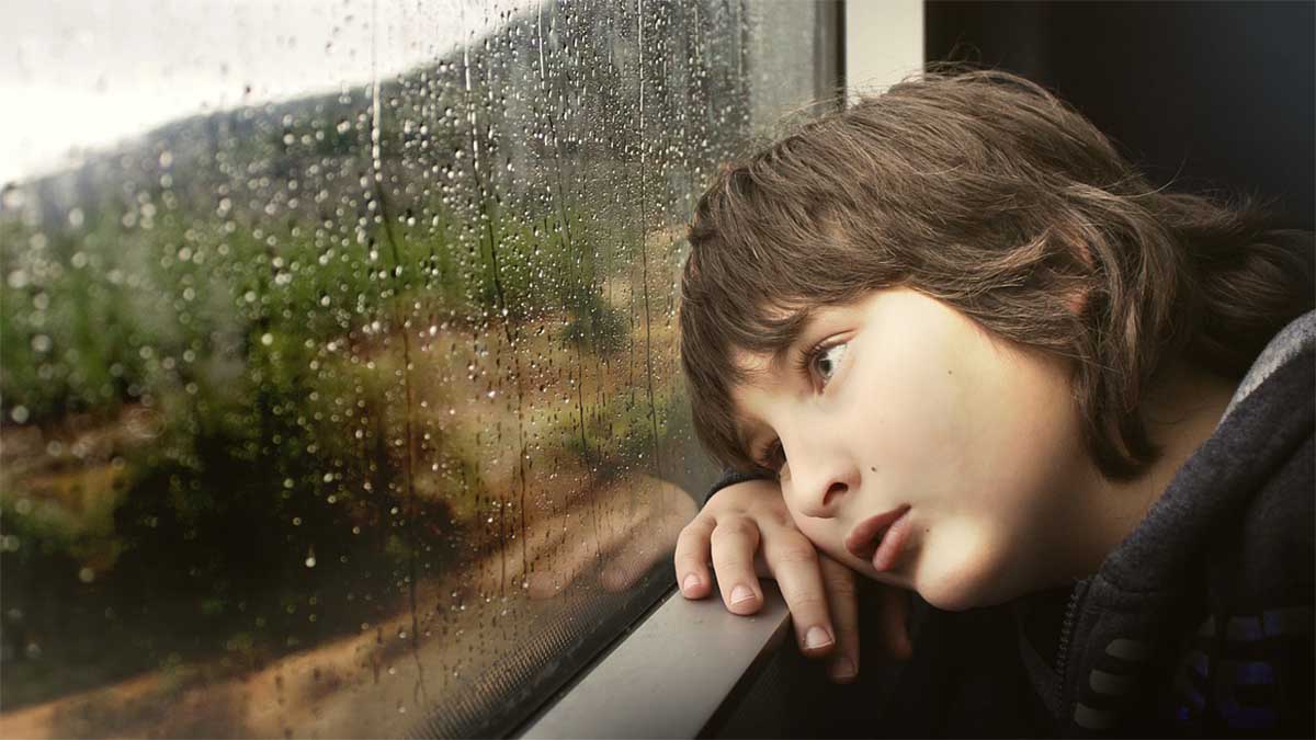 junge schaut traurig aus dem fenster