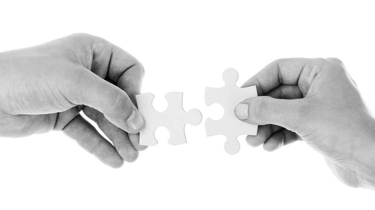 zwei-menschen-haende-stecken-puzzleteil-zusammen