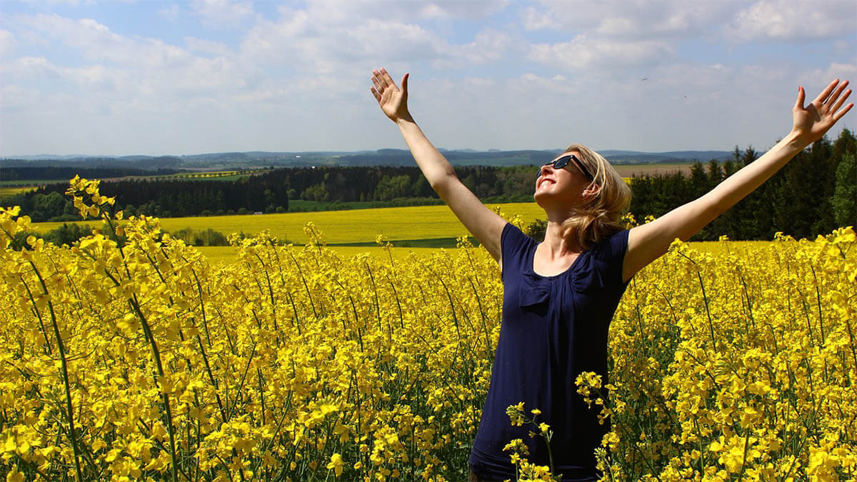 frau-gluecklich-blumenfeld-haende-in-die-luft