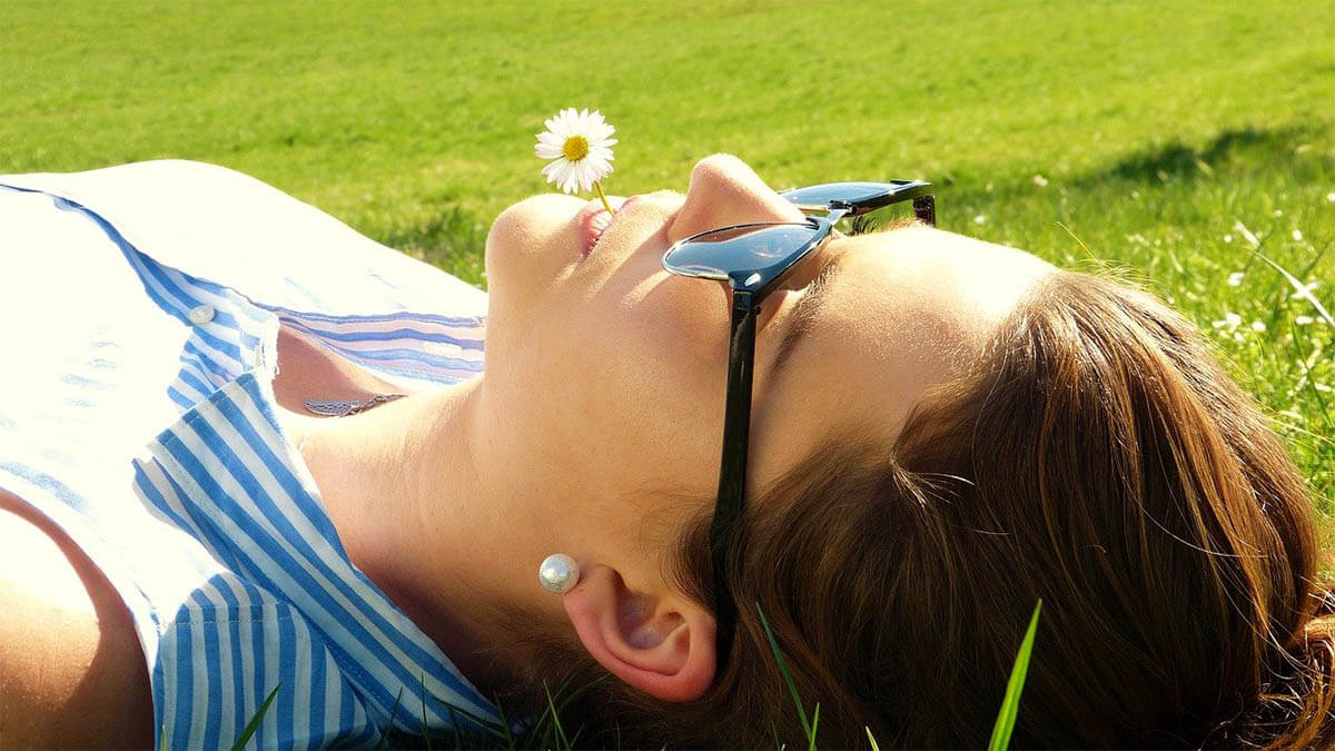 frau-entspannt-auf-wiese-mit-blume-im-mund